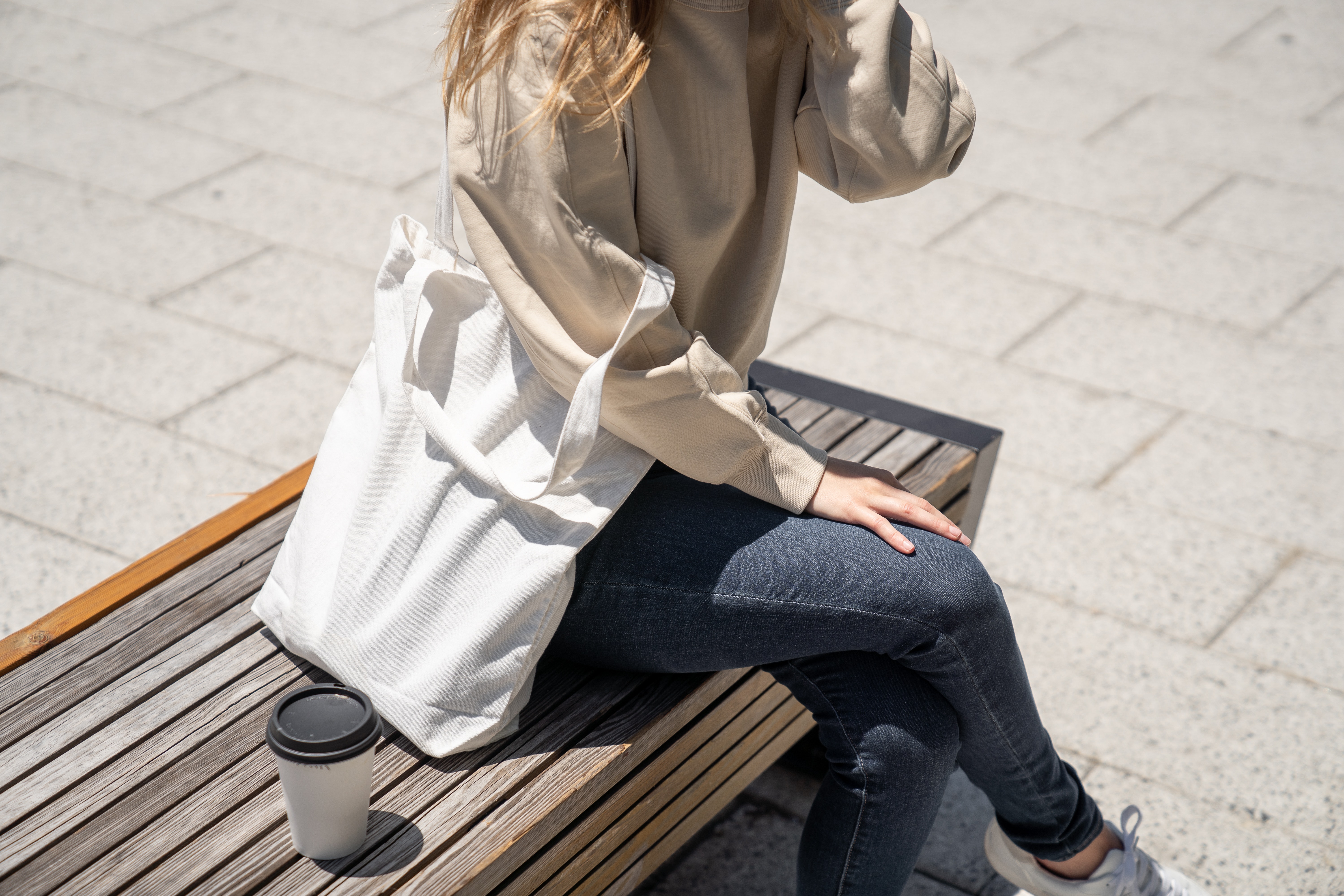 A woman sitting on a bench with a tote bag on her shoulder